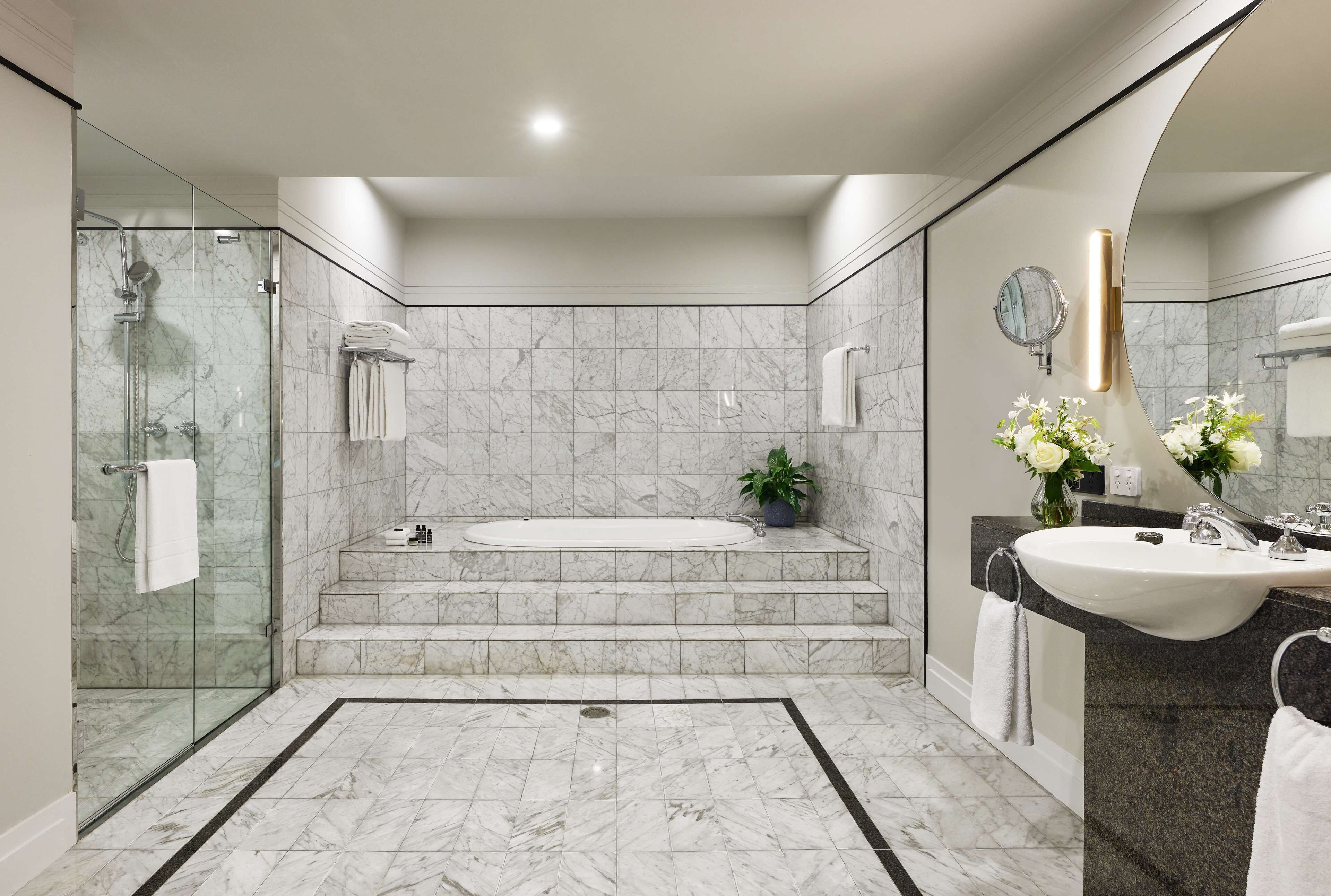 Un baño moderno con ducha envuelta en vidrio, una bañera independiente, tocador con lavabo y un espejo.