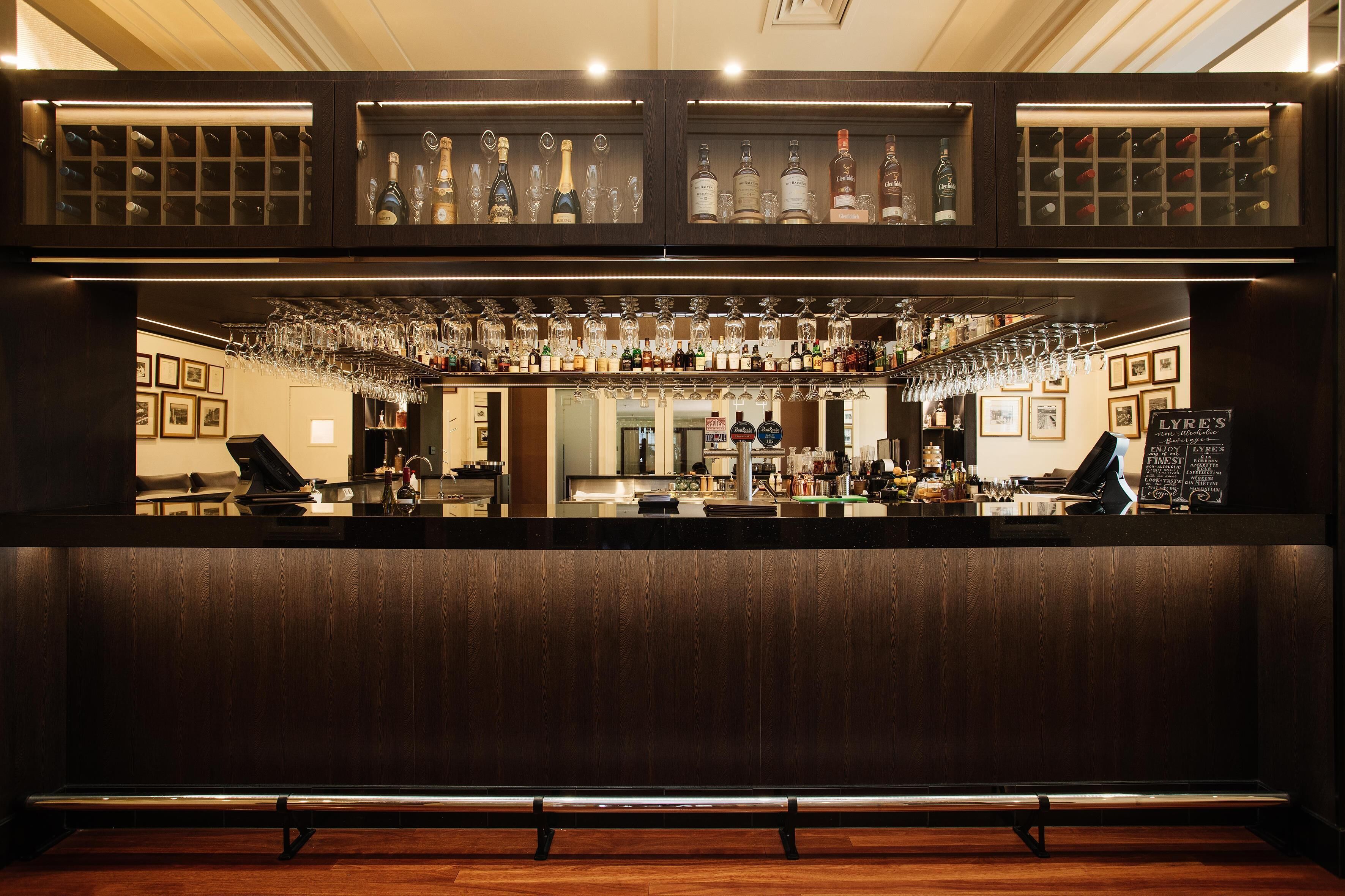A bar area with a wooden counter, shelves with bottles, and hanging glasses.