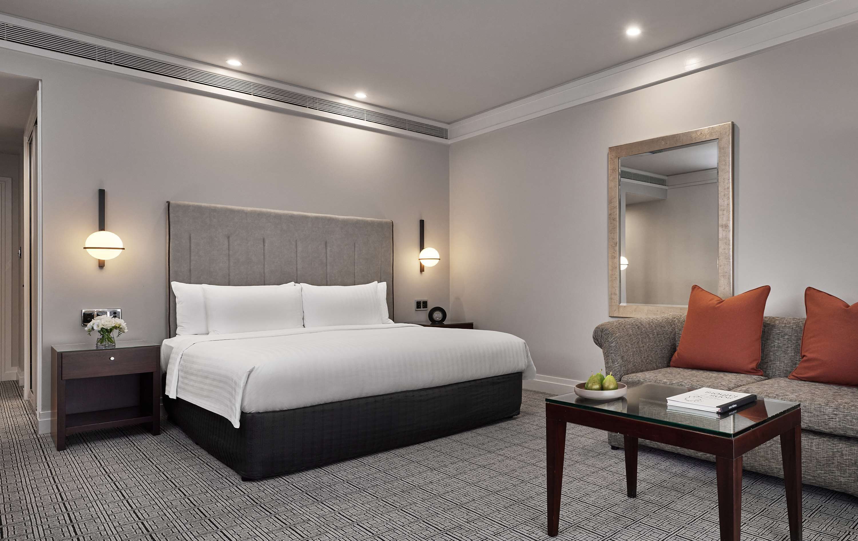 A modern hotel room with a large bed, bedside tables, a sofa, and a glass coffee table.