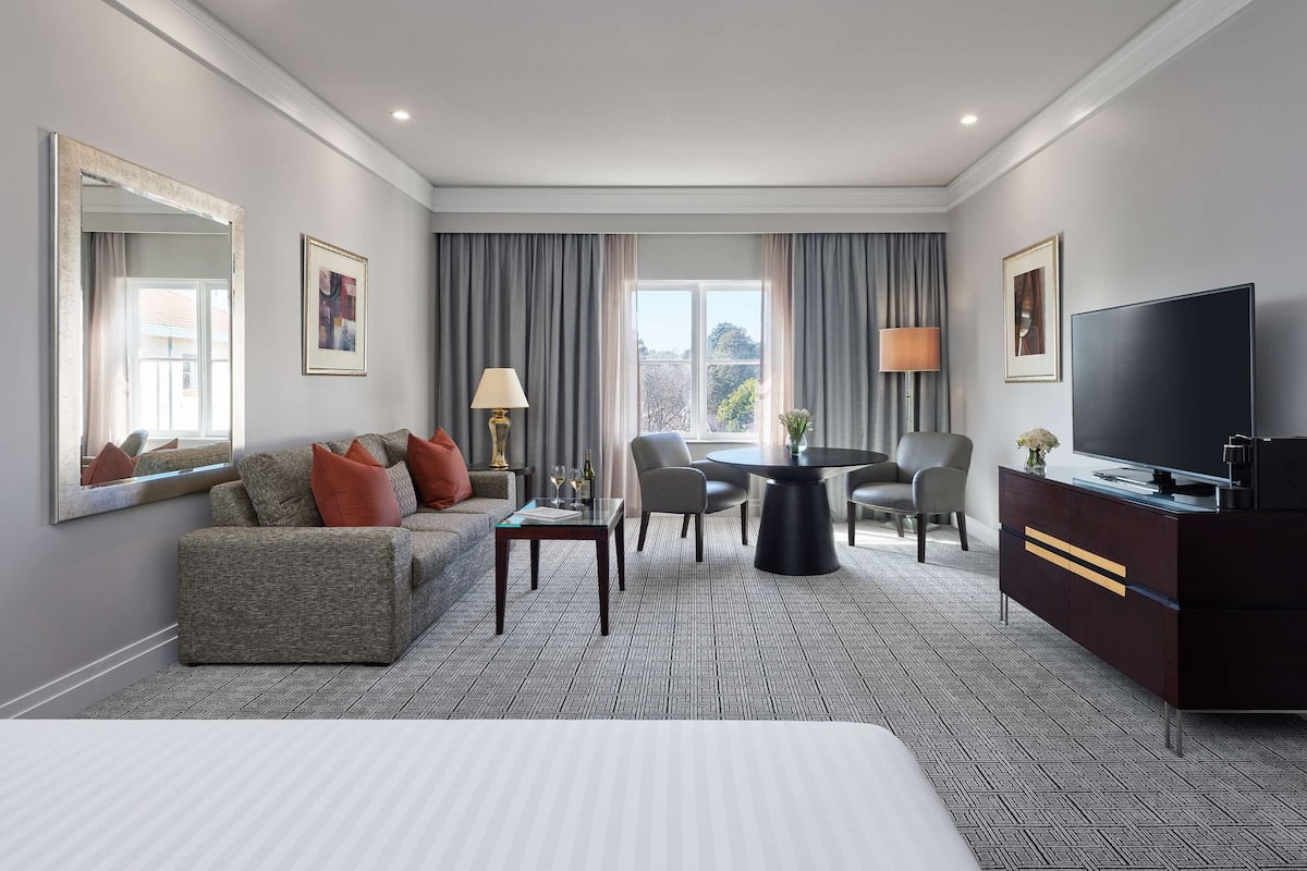 Een hotelkamer met een groot bed, een bank, een eettafel, een televisie en een raam met gordijnen.