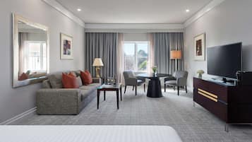 Una habitación de hotel con una cama grande, un sofá, una mesa de comedor, un televisor y una ventana con cortinas.