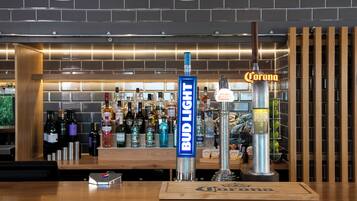 A bar area with a Bud Light tap and a Corona tap, surrounded by various bottles and a wooden counter.