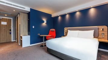 Quarto de hotel com cama, escrivaninha, cadeira e armário.