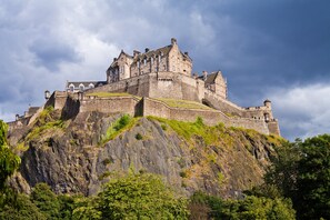 Eine historische Burg auf einem Hügel mit einer befestigten Mauer, steilem Felsgelände und üppiger Vegetation.