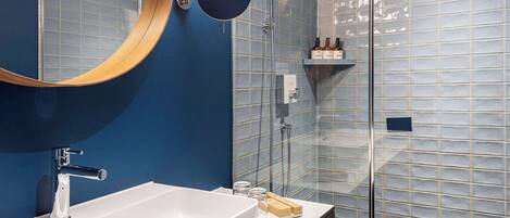 Une salle de bain moderne avec un lavabo blanc, un miroir rond et une cabine de douche en verre.