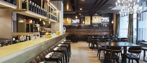 A bar area with stools, a counter with bottles, and a TV screen in the background.