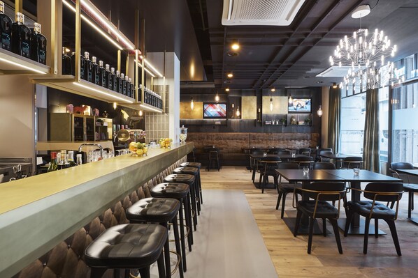 A bar area with stools, a counter with bottles, and a TV screen in the background.
