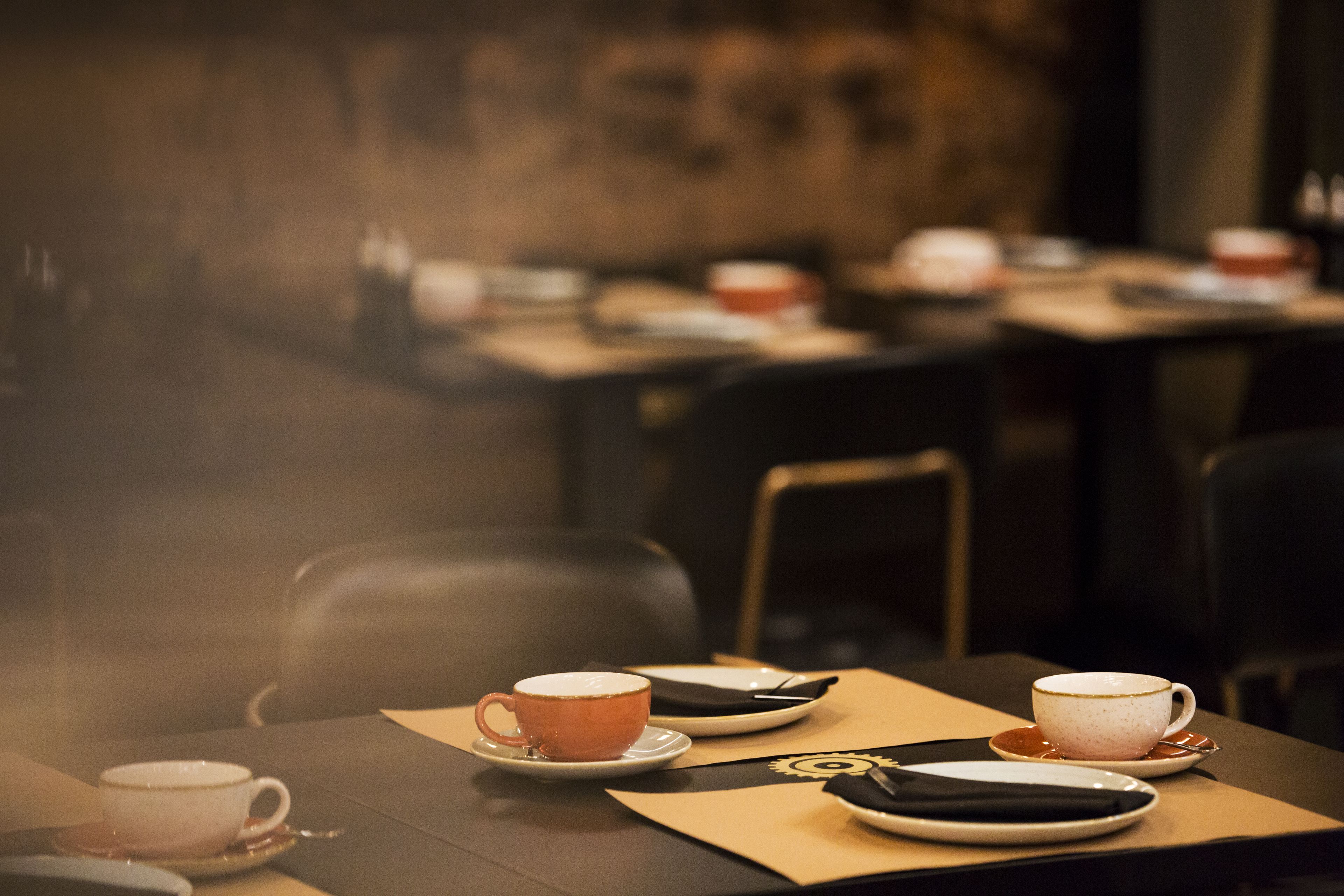 Une salle de restaurant avec des tables mises pour le service, comprenant des assiettes, des verres et des couverts.