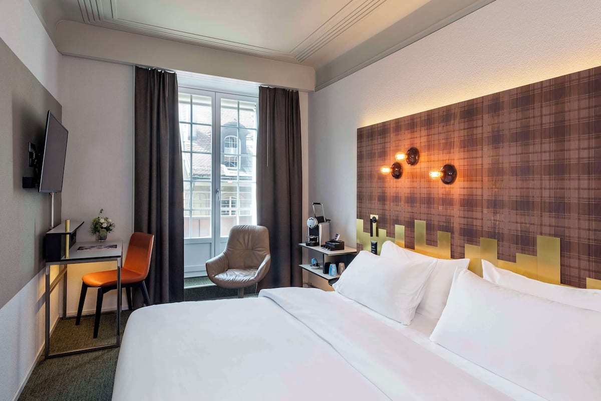Camera d'albergo con un letto grande, una scrivania con una sedia, una televisione e una finestra con tende.