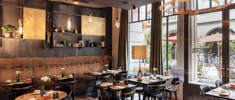 A restaurant with round tables, black chairs, and hanging light fixtures.