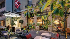 An outdoor cafe with tables and chairs, a British flag, and a building with a sign reading "The Bristol". - NH Bern The Bristol (Bern)