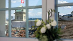 A view through a window of a building with a Swiss flag, a dome, and a mountainous landscape. - NH Bern The Bristol (Bern)