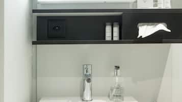 Une salle de bain avec un lavabo blanc, un miroir au-dessus, et une étagère noire contenant des articles de toilette, notamment un flacon de savon liquide.