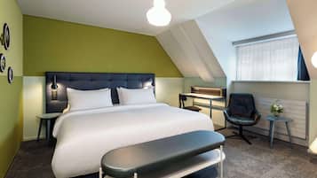 A modern hotel room with a large bed, a desk, a chair, and a small table with a vase of flowers.