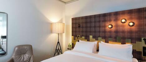 A hotel room with a bed, a chair, a lamp, and a wall with three light fixtures.