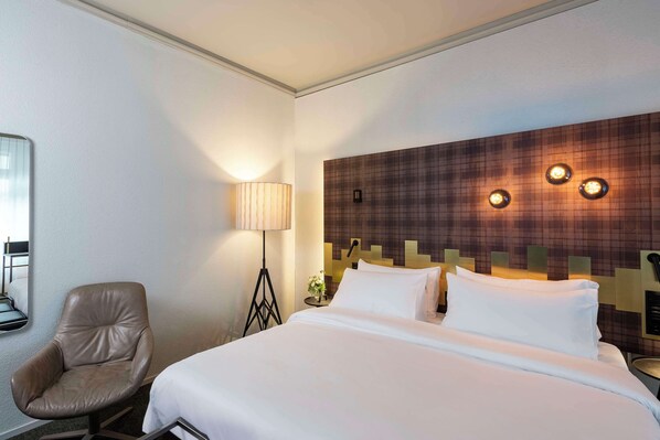 A hotel room with a bed, a chair, a lamp, and a wall with three light fixtures.
