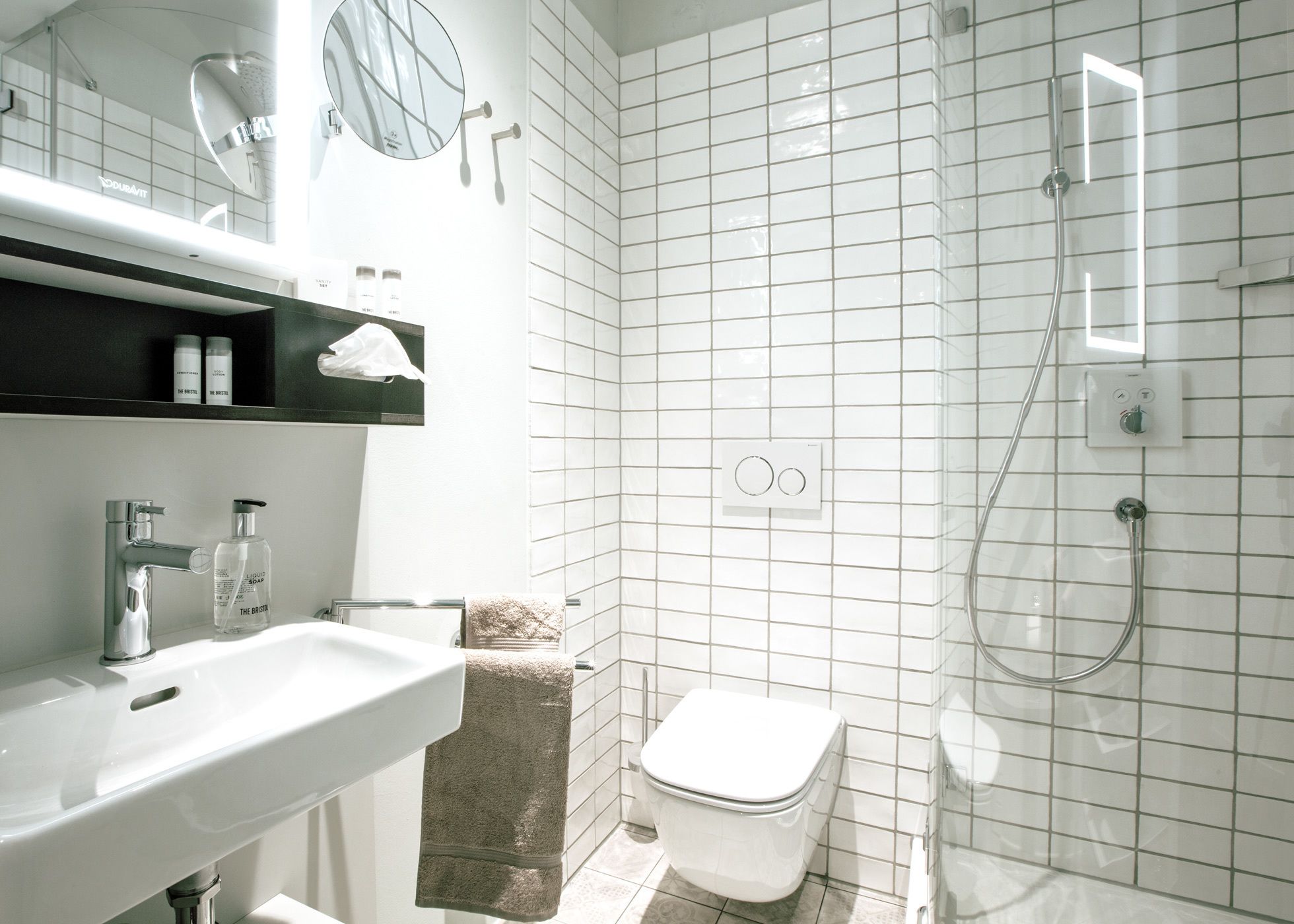 Un baño moderno con lavamanos, espejo y ducha blancos.