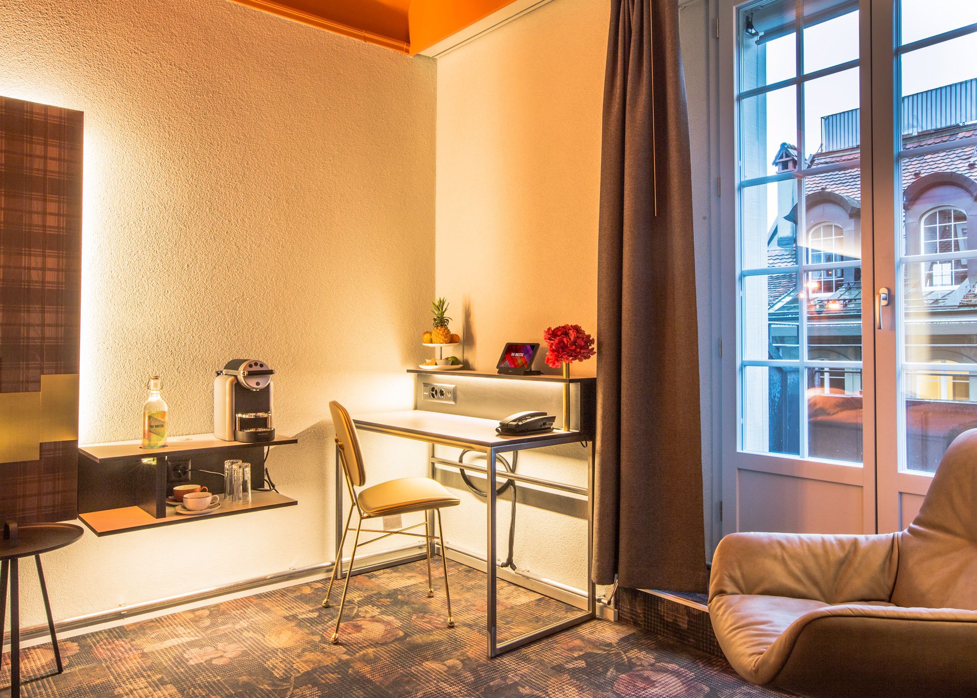 Habitación de hotel compacta con kitchenette, zona de comedor y rincón de estar junto a una ventana con vistas a la ciudad.