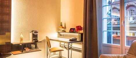 Habitación de hotel compacta con kitchenette, zona de comedor y rincón de estar junto a una ventana con vistas a la ciudad.