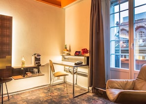 A compact hotel room with a kitchenette, a dining area, and a seating space by a window with a city view.