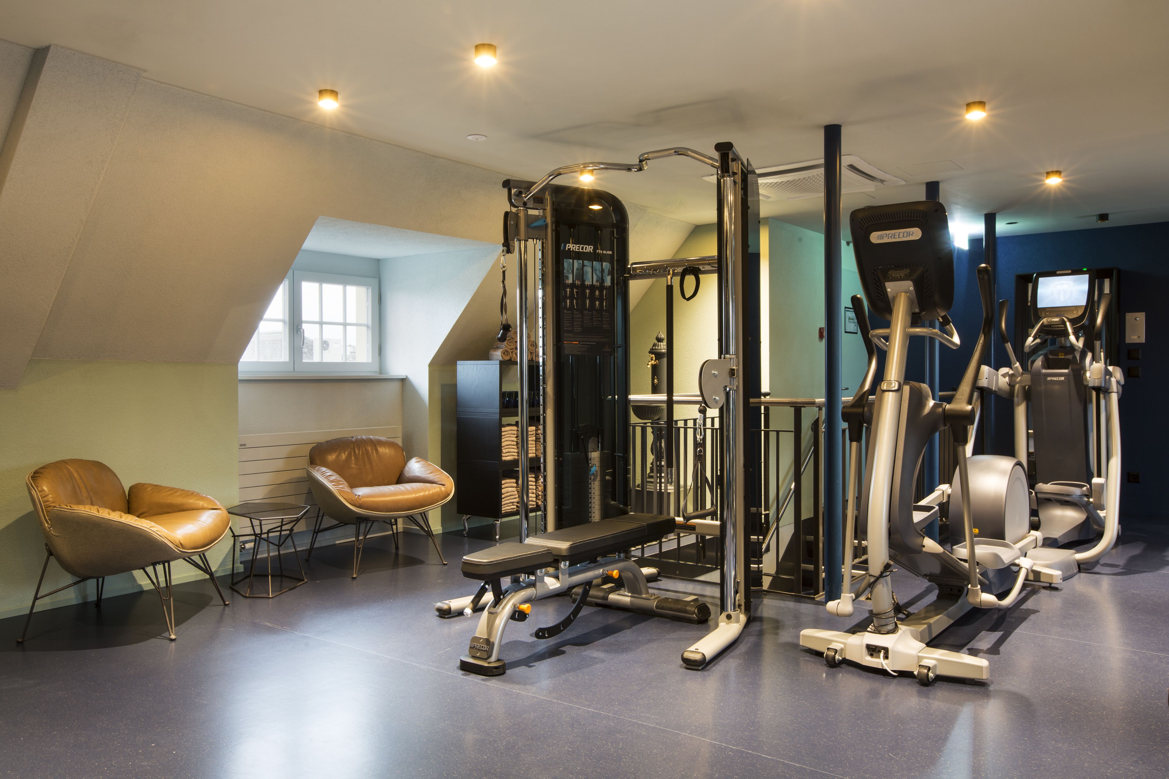 A gym with exercise equipment, a bench, and two leather chairs.