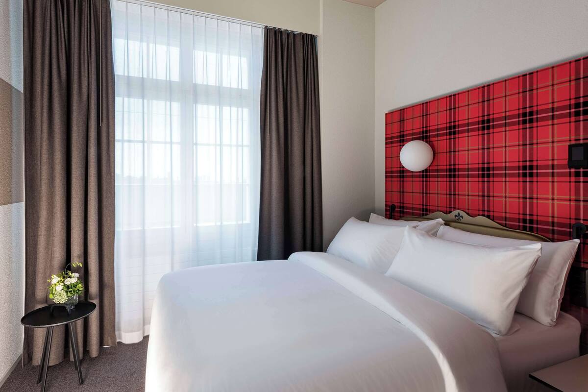 Camera d'hotel con un letto grande, un tavolino con un vaso di fiori e una testiera a rombi rossi.