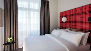 A hotel room with a large bed, a small table with a vase of flowers, and a red plaid headboard.