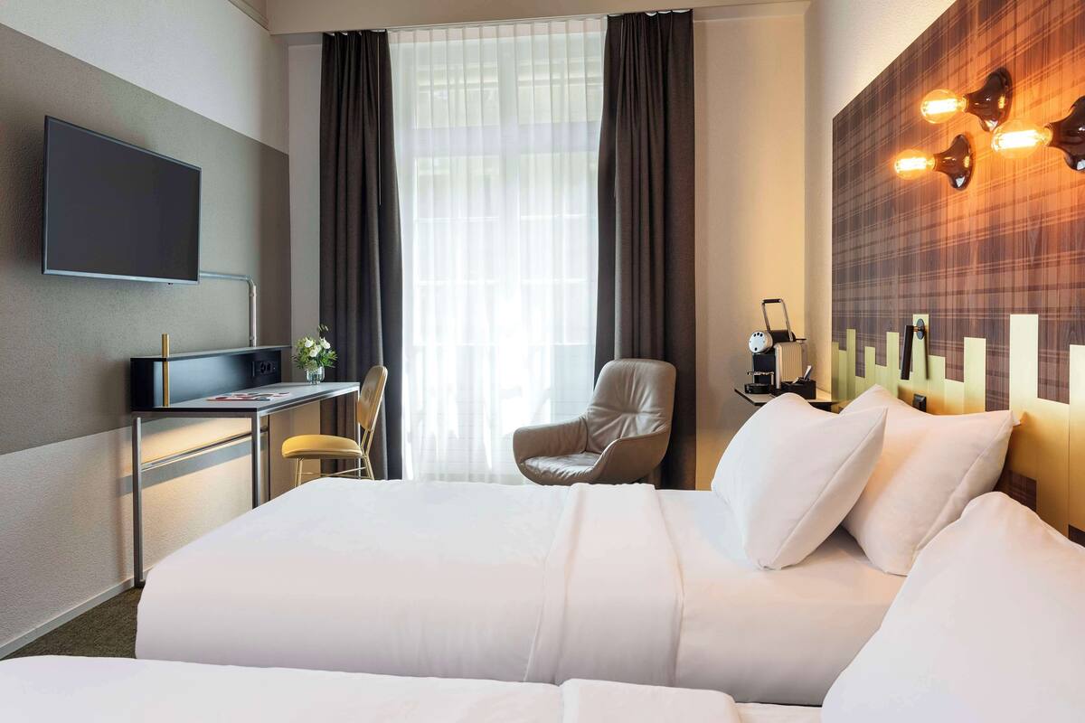 Camera d'albergo con un letto grande, una scrivania con televisore a schermo piatto, una sedia e un punto luce a parete.