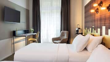 A hotel room with a large bed, a desk with a flat-screen TV, a chair, and a wall-mounted light fixture.