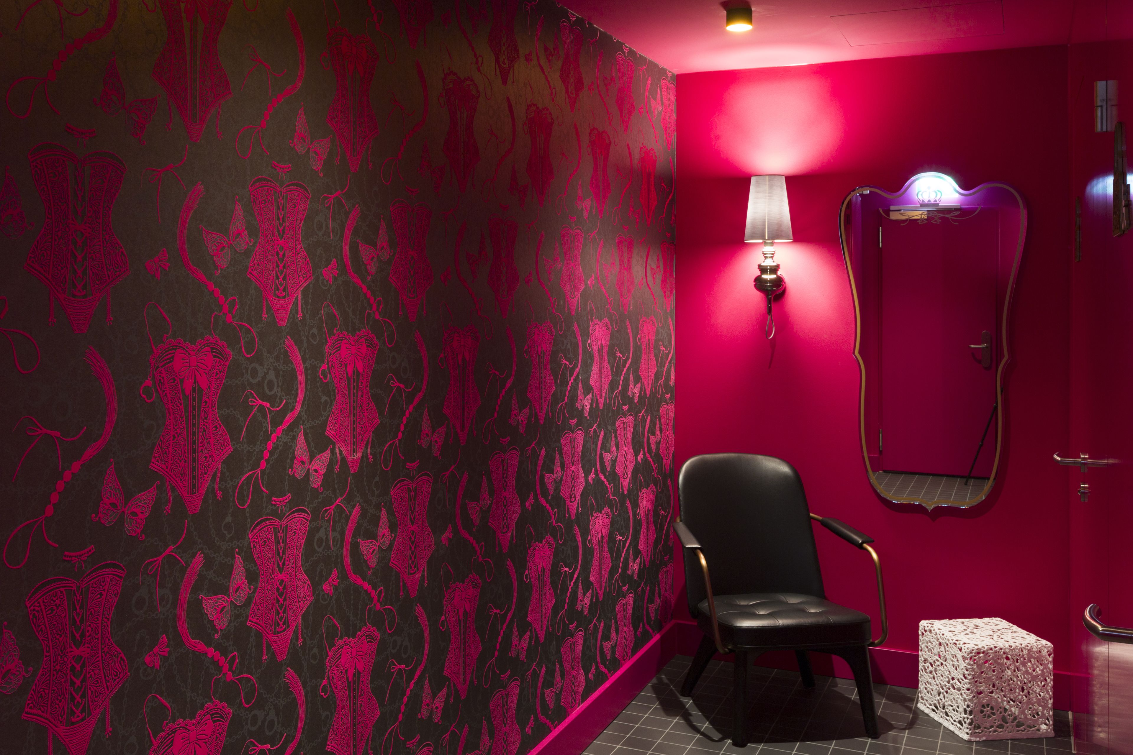 Une pièce avec un mur rouge, une chaise noire, un cube blanc et un miroir.