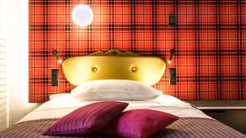 A bed with a gold headboard, white and purple pillows, and a plaid-patterned wall behind it.