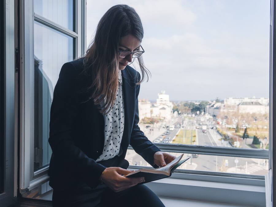 A person sitting by a window with a view of a cityscape.
