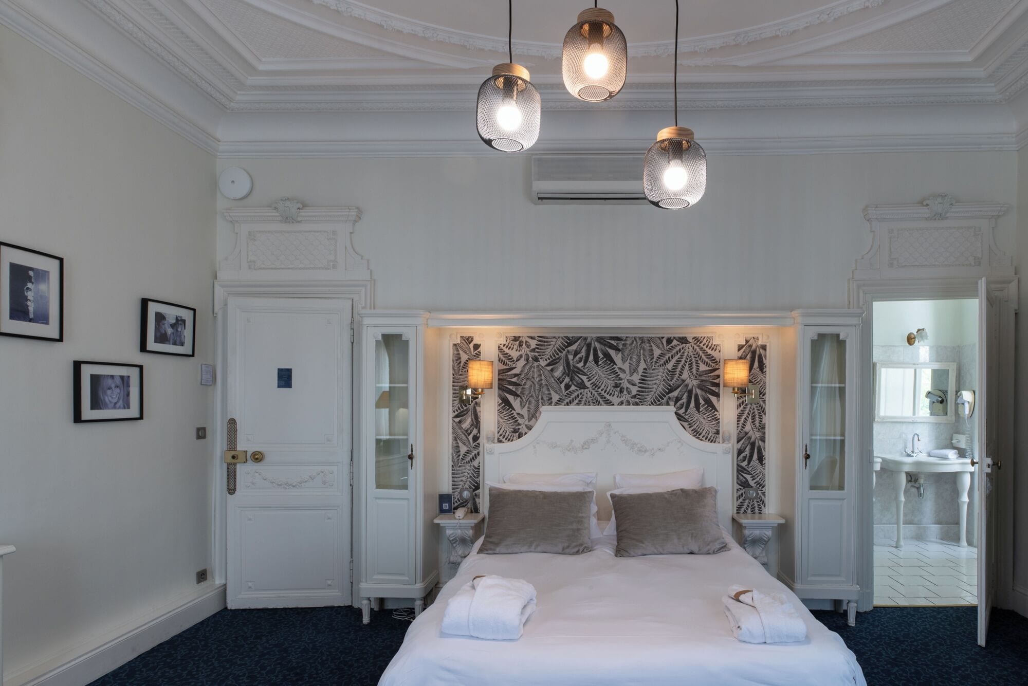 A hotel room with a large bed, a decorative headboard, a nightstand, a bedside table, and a mirror.