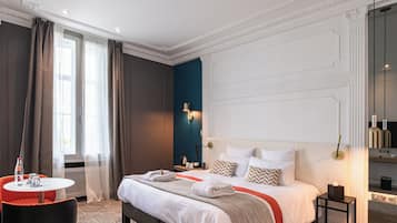 Una habitación de hotel con una cama grande, una mesita de noche, una pequeña mesa redonda con una botella y vasos, y una ventana con cortinas.