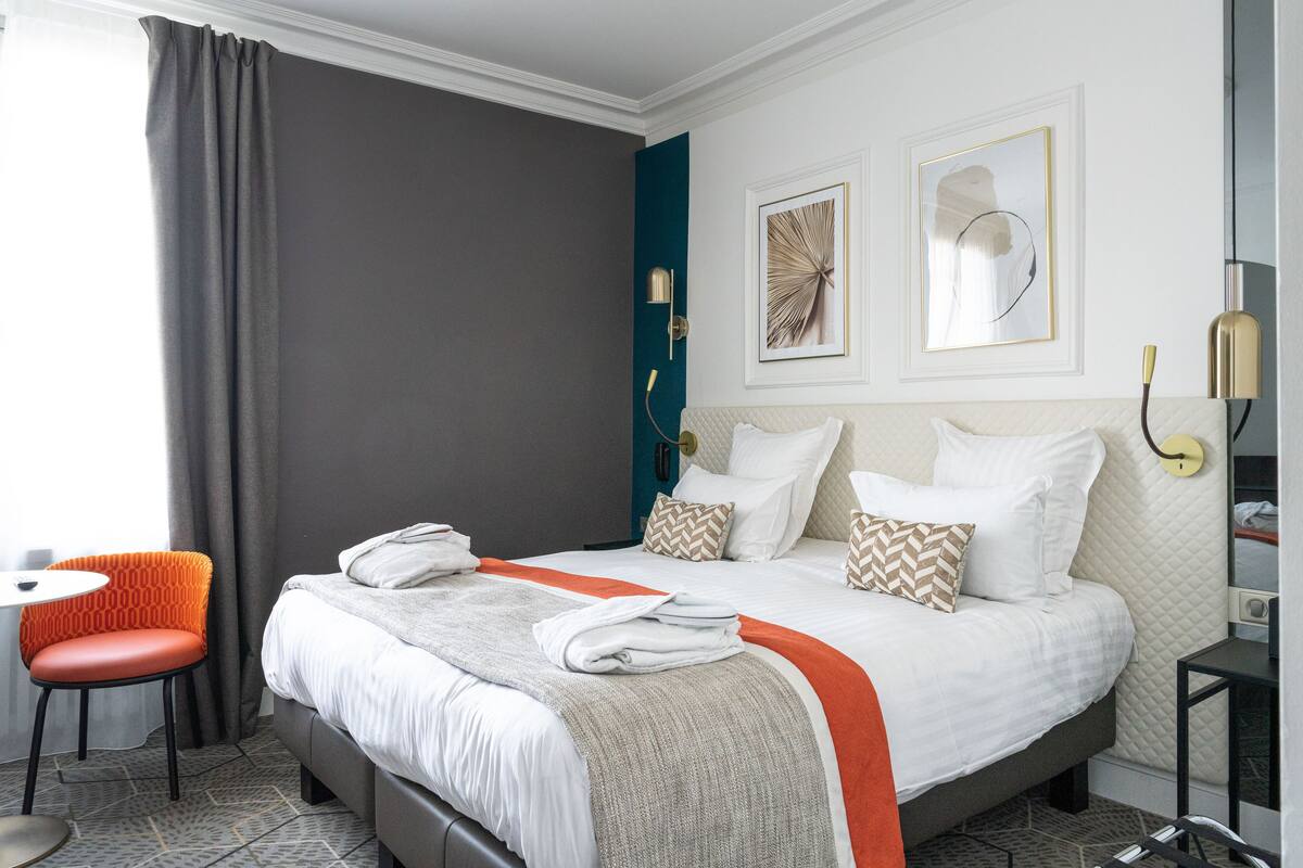 Habitación de hotel con una cama grande, una silla, una mesita de noche y una lámpara fijada a la pared.