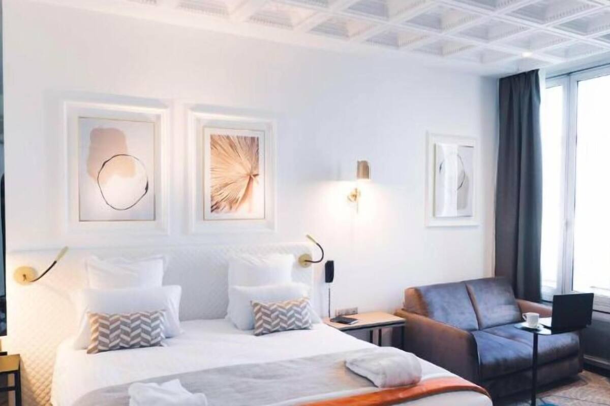 Una habitación de hotel moderna con una cama grande, un sofá y un escritorio. Hay obras de arte enmarcadas en la pared y una ventana con cortinas.