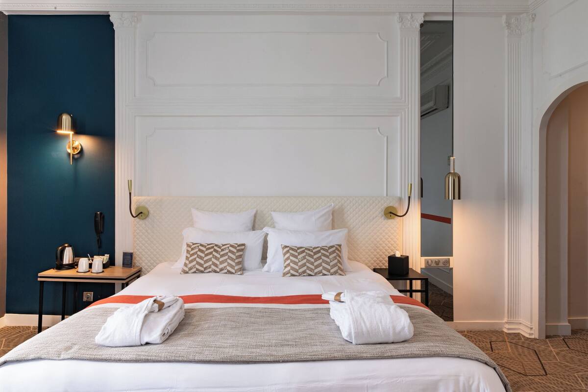 Habitación de hotel con una cama grande, dos mesitas de noche, un teléfono y una lámpara fijada a la pared.