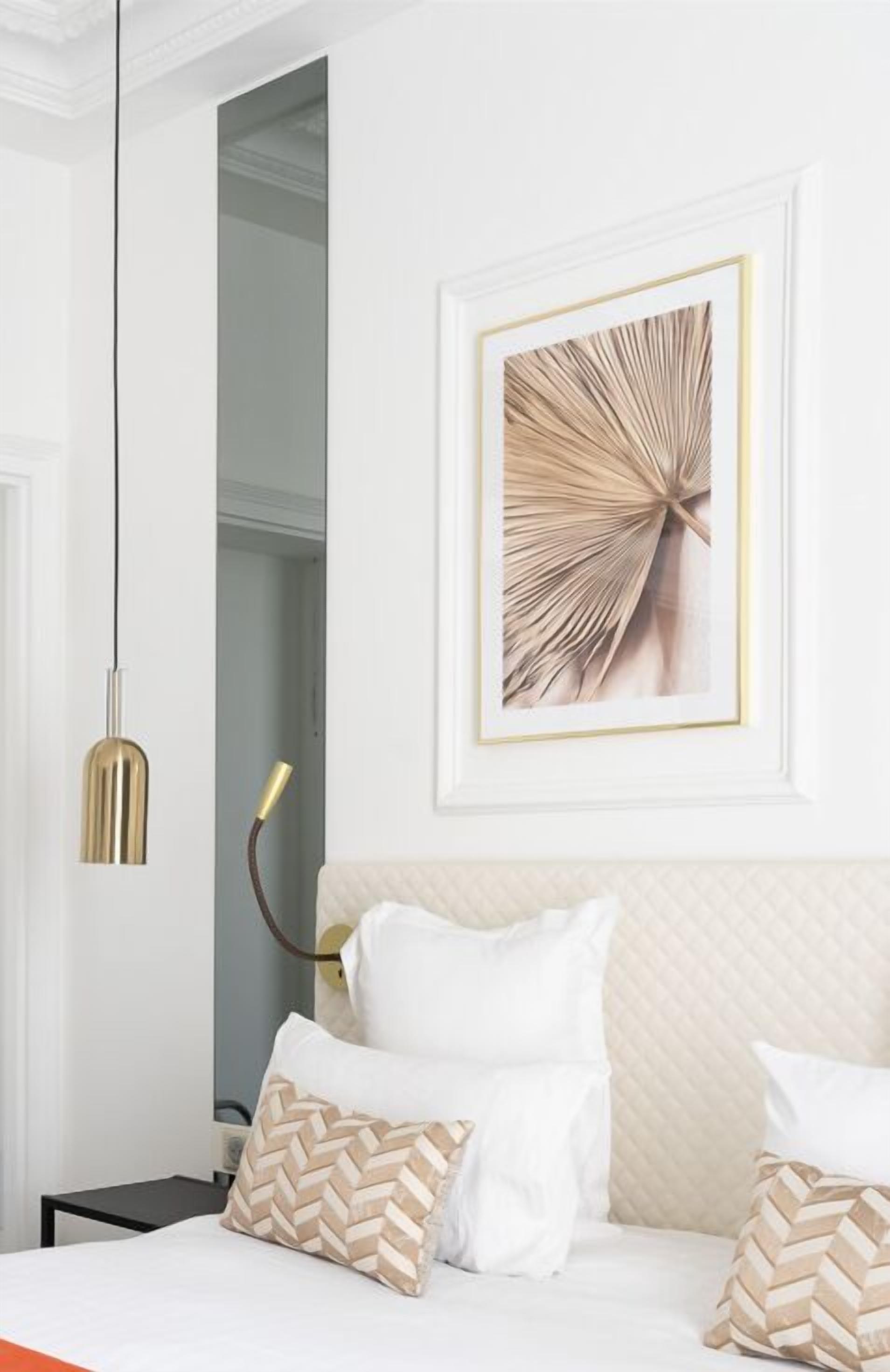 A neatly arranged bedroom with a bed, pillows, a framed artwork, and a pendant light.