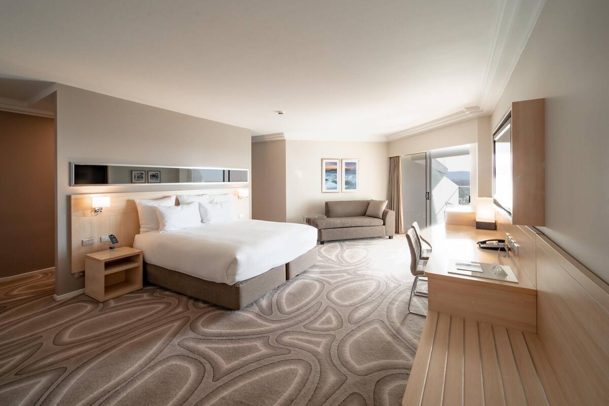 Una habitación de hotel con cama, escritorio, silla, sofá y un ventanal grande.