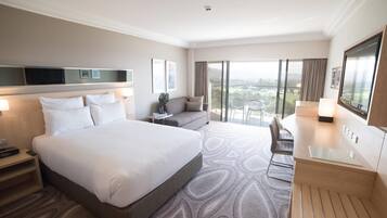 Habitación de hotel con una cama grande, un escritorio, una silla, un televisor y un balcón con vistas.
