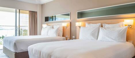 Habitación de hotel con dos camas, un ventanal grande con cortinas y vistas a la ciudad, con un diseño moderno.