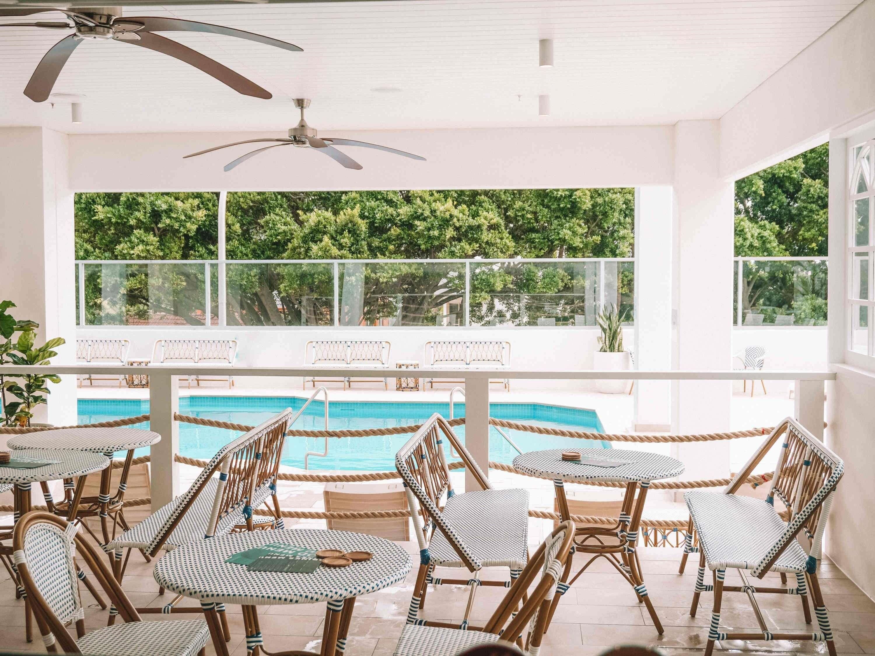 Ein Poolbereich mit Korbmöbeln, einem Deckenventilator und Blick auf den Pool.
