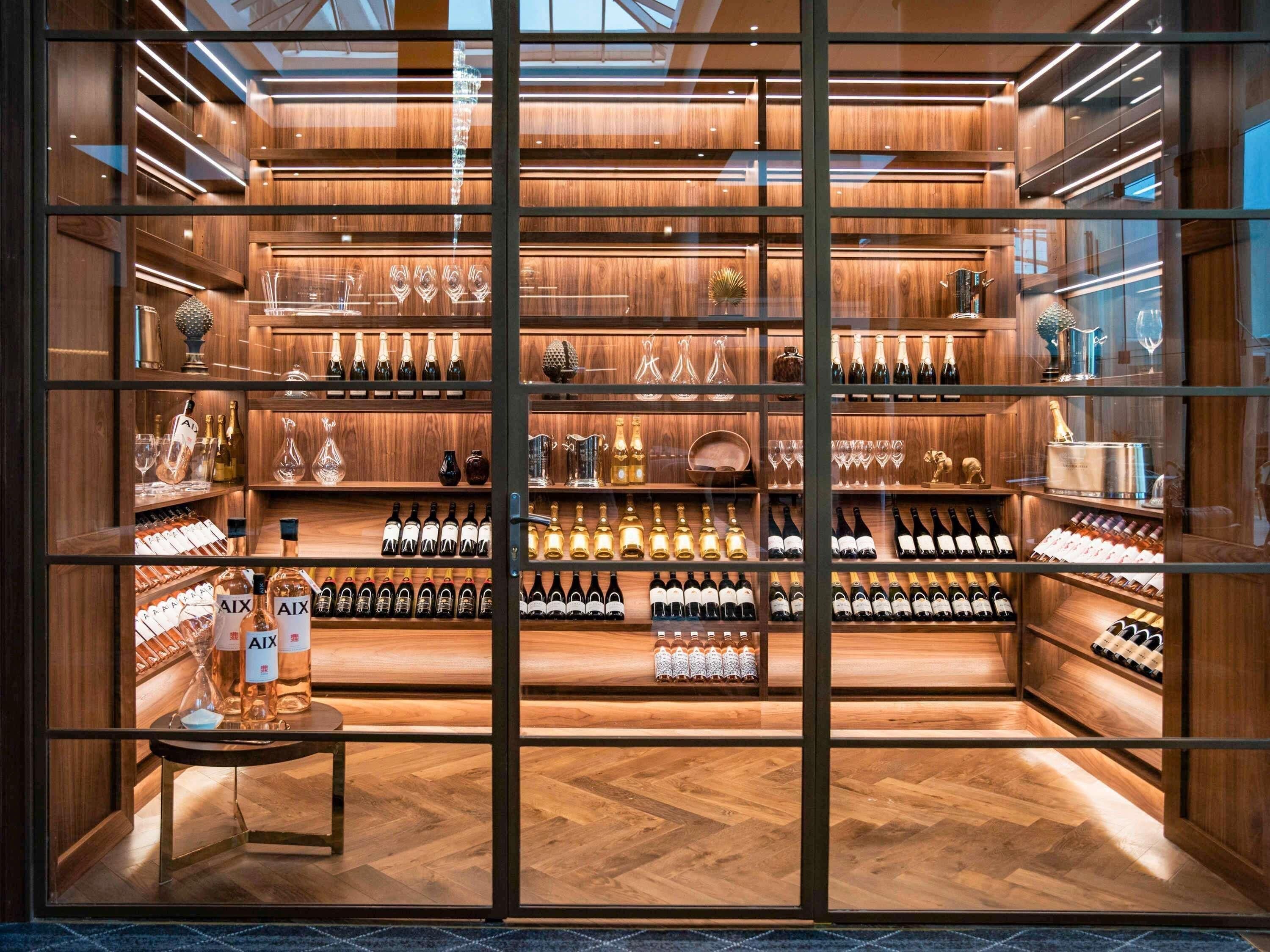 Una bodega con estantes de madera y puertas de cristal, mostrando diversas botellas y cristalería.