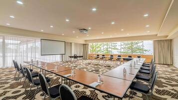 Un salón de conferencias con una larga mesa, sillas, una pantalla de proyector y un amplio ventanal con vistas.