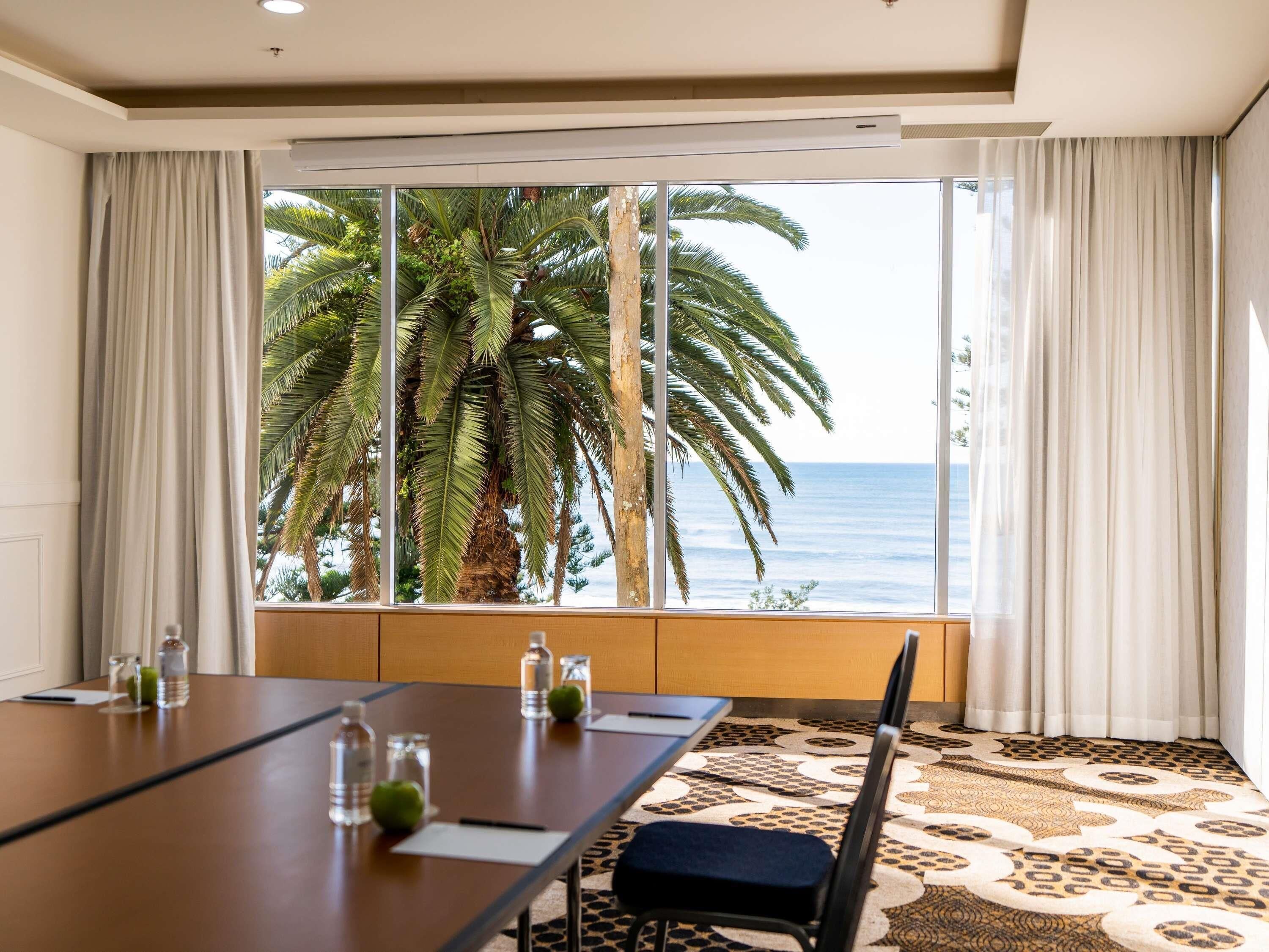 Habitación de hotel con un ventanal grande, una mesa de conferencias y una alfombra estampada.