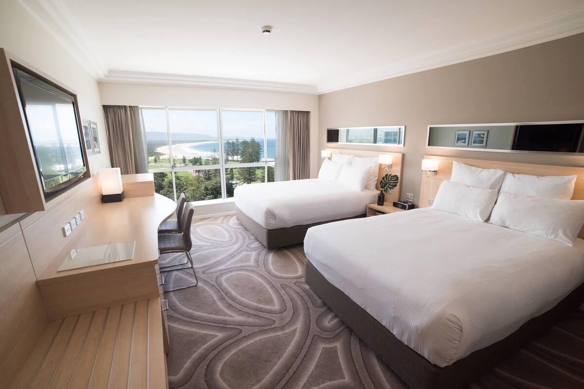 Habitación de hotel con dos camas, un escritorio y vistas al exterior.
