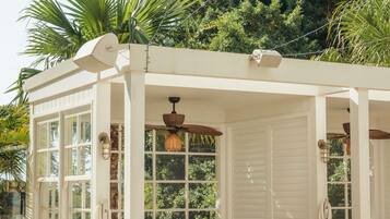 A white gazebo with large windows, a ceiling fan, and a view of lush greenery.