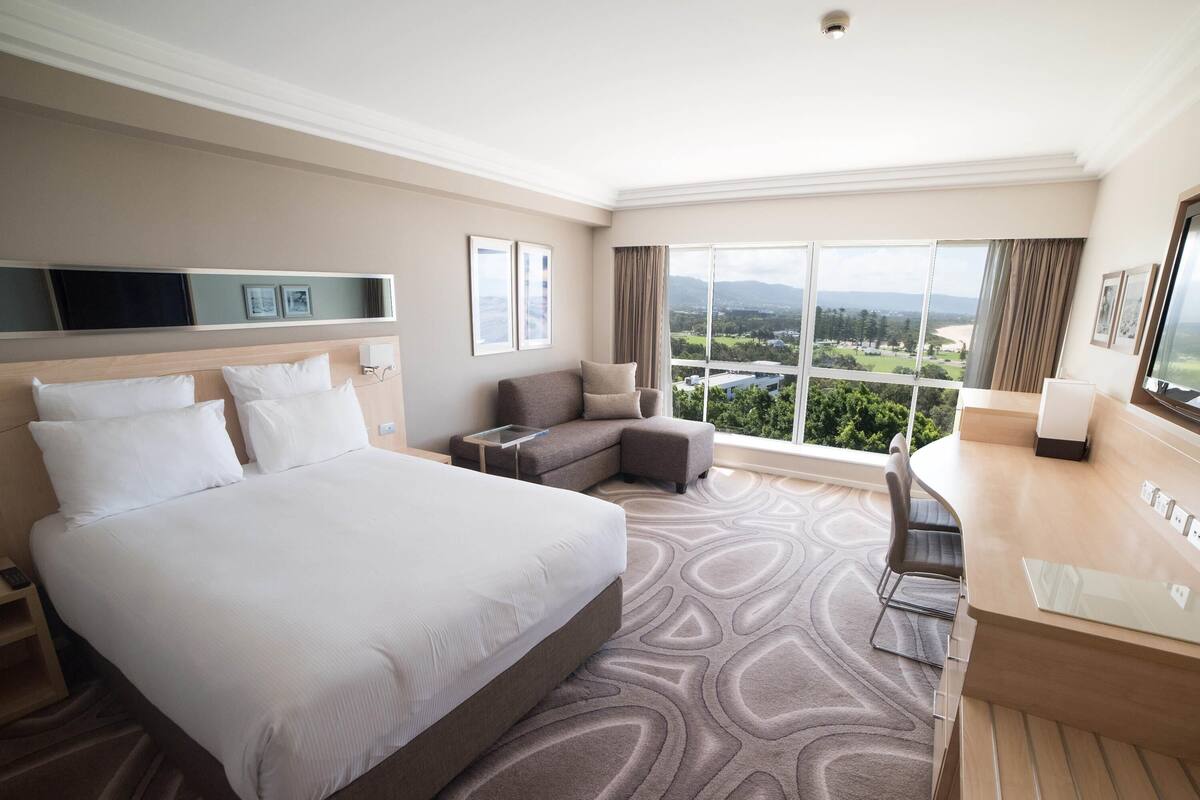 Habitación de hotel con una cama grande, un sofá, un escritorio y vistas al exterior.