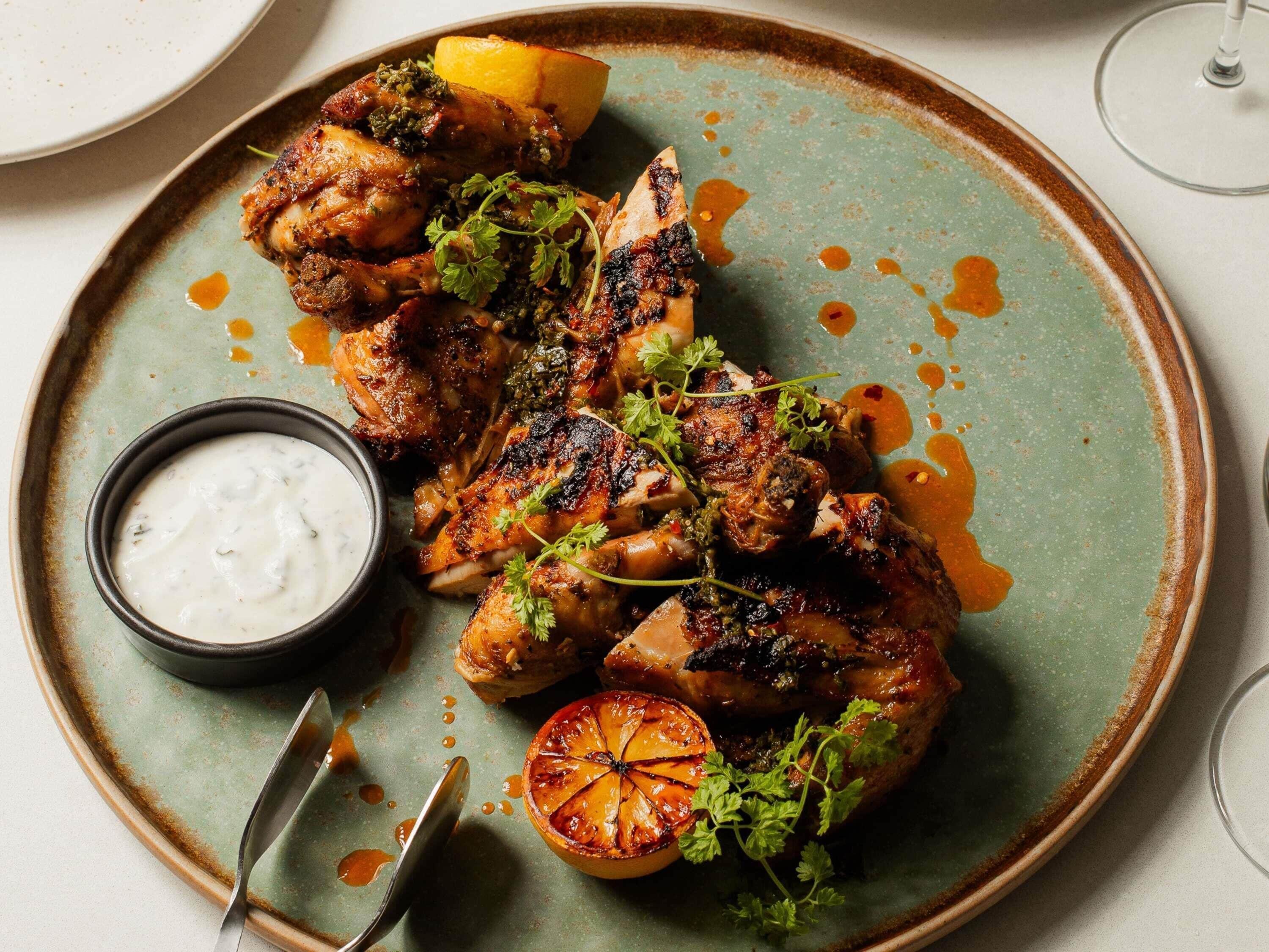 A plate of grilled chicken with a side of sauce and a slice of grilled fruit.