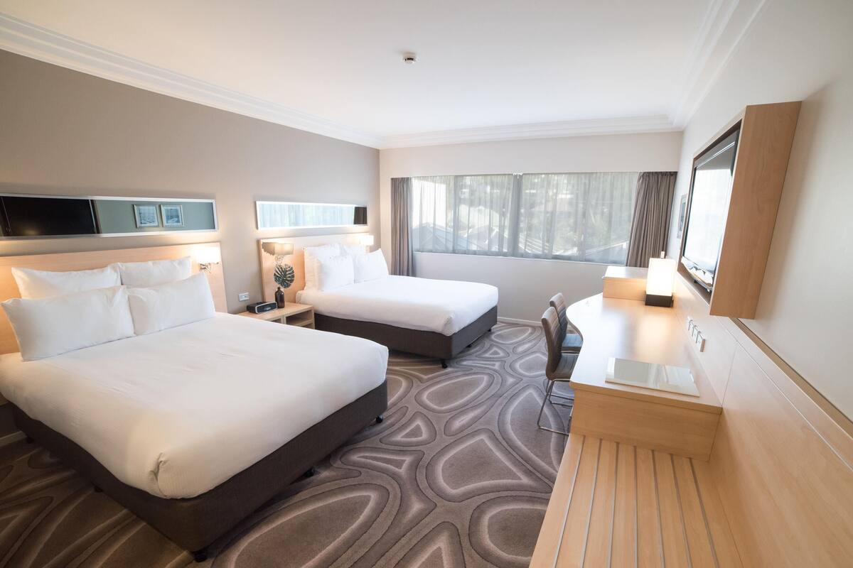 Habitación de hotel con dos camas, un escritorio, un televisor y una ventana con cortinas.